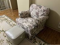 Floral print loveseat with rolled arms positioned near a wall on wood flooring, with a light-colored ottoman in front on a floral area rug.