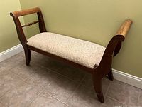 Front and side view of the wooden bench with padded seat and curved arms, showing patterned upholstery and spindle back detail.