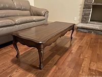 Side angle view of wooden coffee table showing carved cabriole leg and polished wood surface.