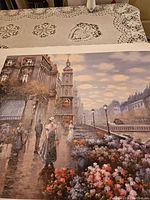 Photo of a large canvas painting depicting a European street scene with bridge, flowers, and figures in period attire.