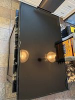 Top view of the TV lying face up on the floor showing the screen and black bezel with a reflective surface.