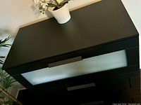 Front view at slight angle showing black-brown finish and frosted glass top drawer.