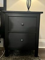 Side view of one IKEA HEMNES black end table showing 2 drawers with round knobs and overall rectangular shape.