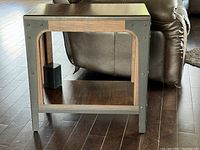 Front view of one solid wood end table showing black metal frame accents and rectangular wooden top and shelf.