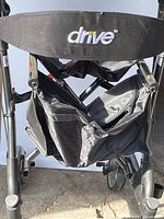 View of the front of the Drive Medical walker, showing black storage bag under the seat with Drive branding embroidered in white and gold.