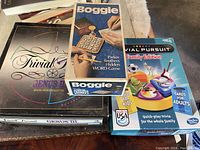 Set of Boggle, Trivial Pursuit Genius III, and Trivial Pursuit Family Edition games shown with their boxes on a table.