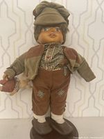 Full frontal view of Camelot hand carved wooden doll Michael, showing detailed facial features and outfit including checkered shirt, brown pants with knee patches, jacket, and cap.