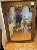 Front view of large mid-century modern style wall mirror showing rectangular shape with arched top and decorative top center motif. Mirror is clear and in very good condition with minor scratches visible on the frame.