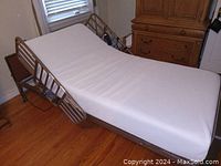 Adjustable hospital bed with white mattress platform raised at head, brown scratch-resistant bed ends, and casters on hardwood floor.