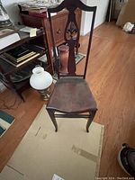 Front angle showing the whole chair, carved wooden backrest, worn wooden seat, and damage to chair base.