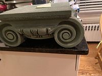 Close-up of one side showing spiral volute details with leaf accents on Ionic style column riser.