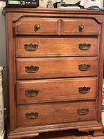 Front view of the tall wooden dresser showing all five drawers with brass hardware, polished wood surface, and overall condition.