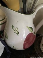 White ceramic water pitcher with hand-painted red apple, green leaves, and white flower decoration.