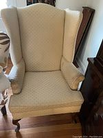 Front view of beige wing back chair showing upholstery, arms, and seat cushion.