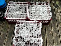 120 clear glass champagne flutes arranged in three red plastic carriers with white grids, visible from above.