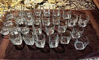 Top-down view showing 28 clear square shot glasses arranged in rows on a towel surface.