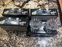 Four black boxes containing two crystal candle holders each, two candle holders placed on top showing the scalloped petal design and transparent crystal material.