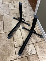 Two black Bike Nook stands set on a tiled floor, showing tripod bases with rubber feet and V-shaped bike holders.