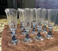 Front view of 14 blue crystal flutes on a brown cloth showing clear fluted bowls with blue accent in stems