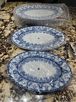 All three porcelain plates with blue and white pattern and assembly hardware on countertop, wrapped in plastic