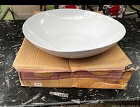 White large round bowl displayed on top of original cardboard box with visible wear and tear.
