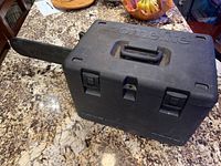 Closed black plastic carrying case with embossed 'Homelite' branding and chainsaw bar partially protruding.