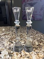 Front view of two crystal candlesticks with conical faceted bases and tapered stems on a granite countertop.