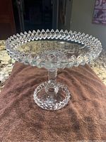 Diamond cut glass pedestal cake tray showing full item on towel and granite surface, clear glass with detailed diamond cuts around rim and base, pedestal stem with ribbing
