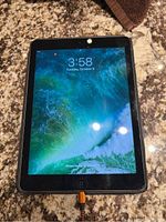 Apple iPad Air powered on showing time and date with orange charging cable connected. Device placed on granite countertop.