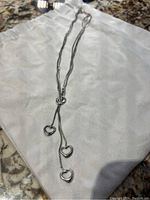 Full view of silver necklace with three heart charms on white cloth background.