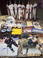 Full view of the sports memorabilia lot arranged on countertop showing baseball cutouts, baseballs, hat, hockey pucks, photos and signed collectibles.