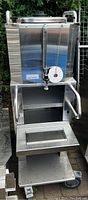 Front view of stainless steel thermal dispenser mounted on rolling shelf cart with drip tray and caster wheels.