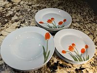 Four stacks of dishes showing orange tulip floral design on white plates and bowls of varying sizes.