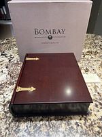Dark brown wooden keepsake box with brass hinges and hardware placed on a granite surface, accompanied by original Bombay Company box in the background.