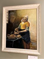 Full view of the framed painting showing a woman in yellow pouring a liquid at a table.