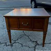Front view of wood side table showing entire piece with drawer and legs against pavement background