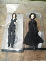 Two Twilight Eclipse Barbie dolls in original plastic window boxes on a wooden floor, one dressed in black vest and pants (Alice) the other in black coat and hood (Jane).