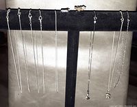 Eight slender sterling silver chains displayed on a black stand, two with small pendants, one shaped like an ice skate and the other star-shaped.