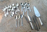 Birks silverplate Old English Regency Plate pie server with various spoons and knives laid out on wood surface, showing all items together, silverplate tarnished and in need of cleaning.