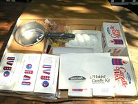 Photo showing open box with all parts of the Skilcraft molded candle making kit neatly arranged inside, including pot, wax boxes, candle mold, instructions, and colorants.