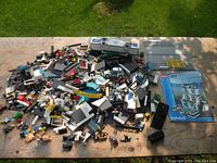 Overview of assorted Lego City pieces and instruction manuals spread on wooden surface outdoors.