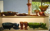 Wide shot of the top and bottom shelves showing a selection of amber, green and blue carnival glass bowls, goblets and vases.