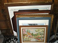 Lot of six large framed pictures stacked together, showing variety of frame styles and sizes