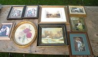 Lot of 10 small framed pictures of children, floral, cabin winter scene, pastoral scene and others on a wooden table outdoors.