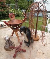 Photo showing the lot of wooden decor items including the elephant tripod bowl stand, wooden penguin, willow tree, small tripod stand and thimble display case on a wooden surface outdoors.
