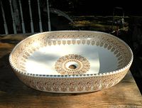 Top view of oval white porcelain sink showing gold mosaic decoration around rim and central drain opening
