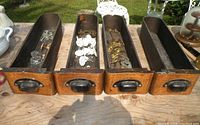 Four wooden sewing machine drawers with various old hardware inside, photographed outdoors on a wooden surface.