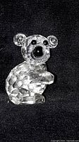 Front view of the clear faceted koala crystal figurine with black eyes and nose on a black background.