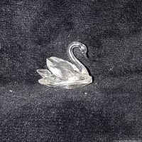 Clear Swarovski crystal mini swan figurine front and side views on black background showing faceted crystal detailing and shape.