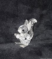 Clear faceted crystal squirrel sitting upright holding a nut, set against a black background.